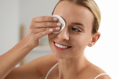 Photo of Smiling woman removing makeup with cotton pad indoors, closeup