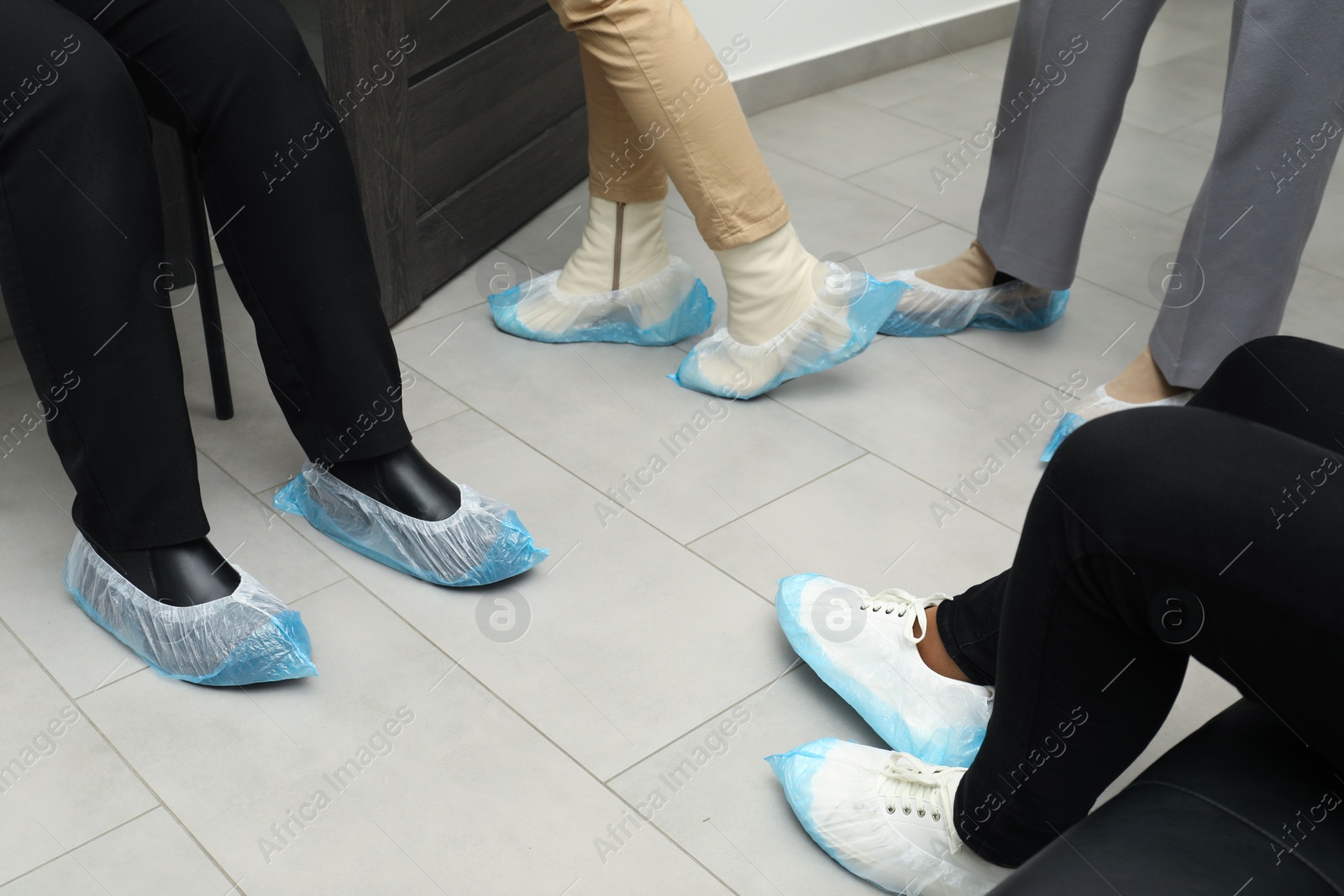 Photo of Women wearing blue shoe covers onto different footwear indoors, closeup