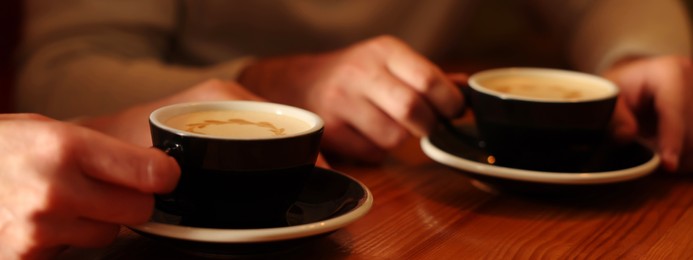 Image of People with cups of aromatic coffee at wooden table, closeup. Banner design