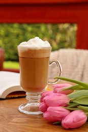 Glass of delicious cocoa and pink tulips on wooden table at balcony