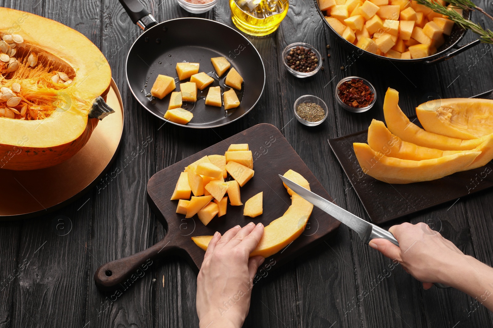 Photo of Woman cutting fresh pumpkin at black wooden table, above view