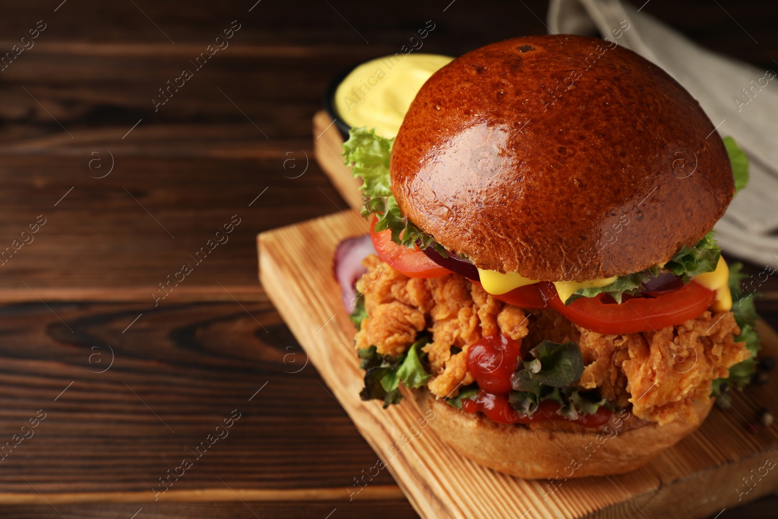 Photo of Delicious burger with crispy chicken patty on wooden table, closeup. Space for text