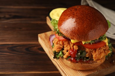 Delicious burger with crispy chicken patty on wooden table, closeup. Space for text
