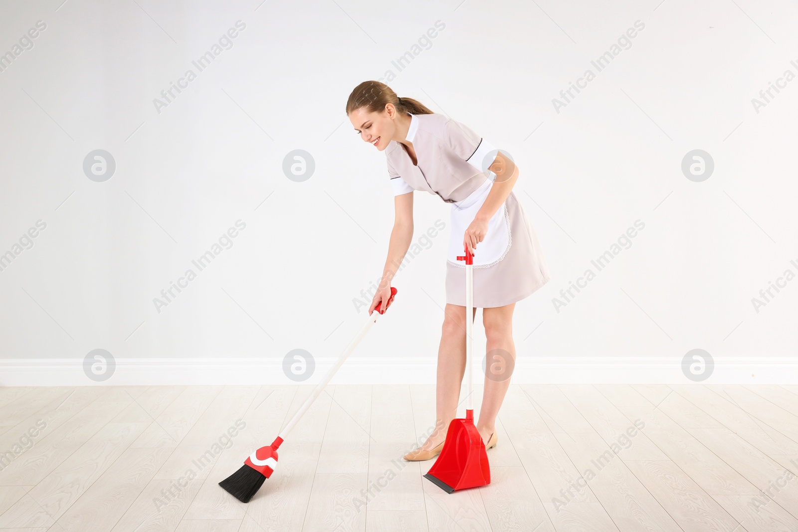 Photo of Young chambermaid with broom and dustpan  indoors