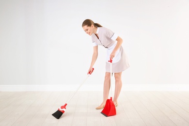 Young chambermaid with broom and dustpan  indoors