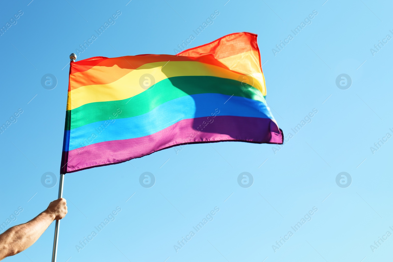 Photo of Gay man holding rainbow LGBT flag on blue sky background