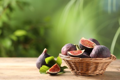 Photo of Wicker bowl with fresh ripe figs and green leaf on wooden table. Space for text