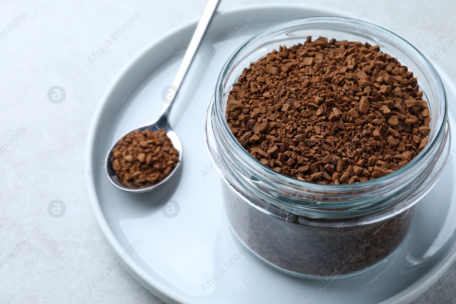 Photo of Spoon and glass jar with instant coffee on light table, closeup