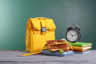 Photo of Composition with lunch box and food on table against blackboard