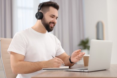 Young man in headphones using video chat during webinar at table in room