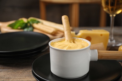 Photo of Pot of tasty cheese fondue and products on wooden table