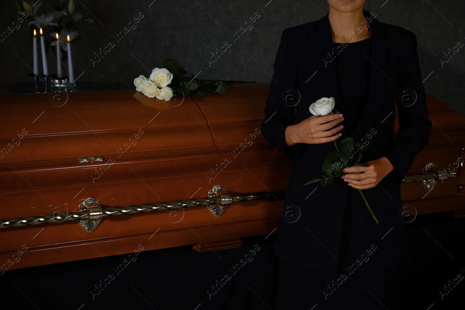 Photo of Young woman with white rose near casket in funeral home, closeup