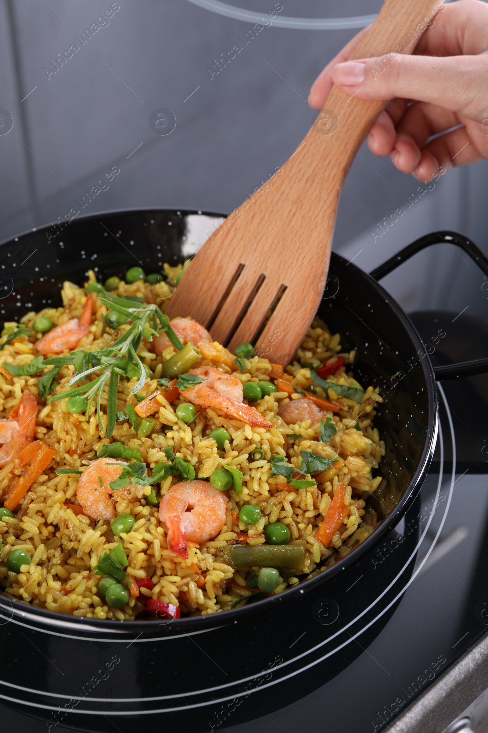 Photo of Woman cooking tasty rice with shrimps and vegetables on induction stove, closeup