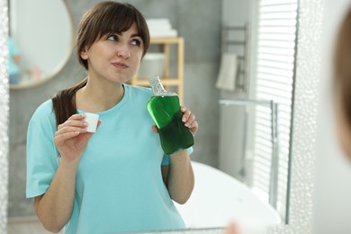 Photo of Young woman using mouthwash near mirror in bathroom, space for text