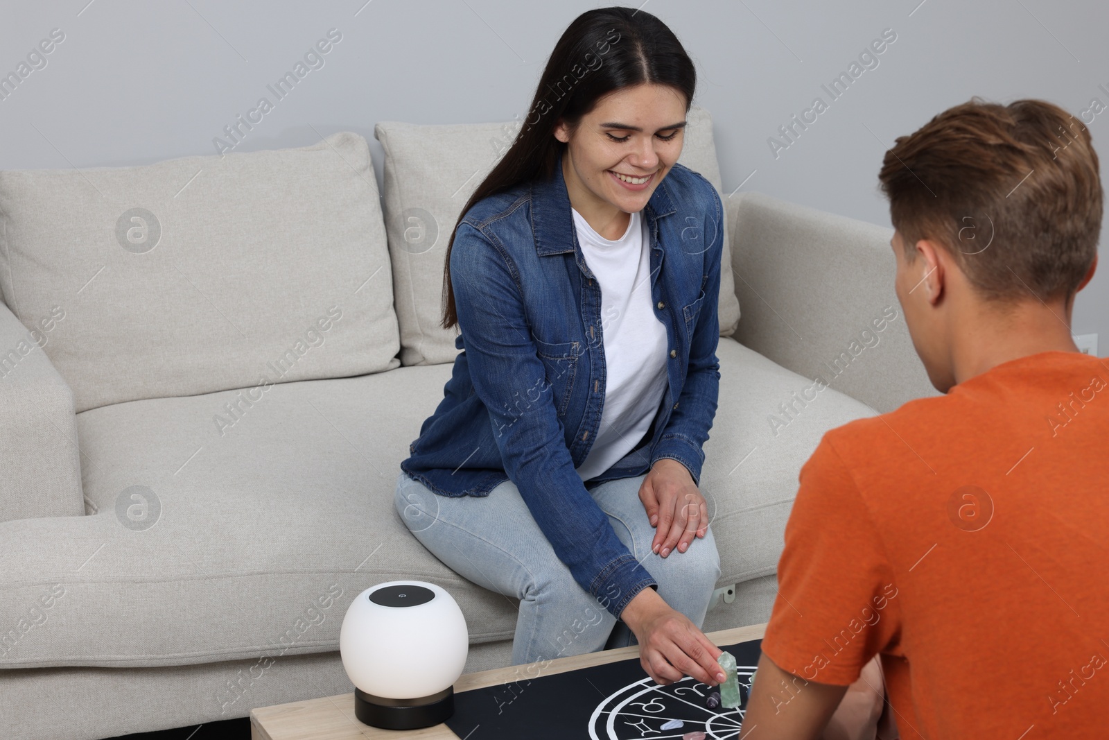 Photo of Astrologer predicting client's future with zodiac wheel, stones and crystals at wooden table indoors