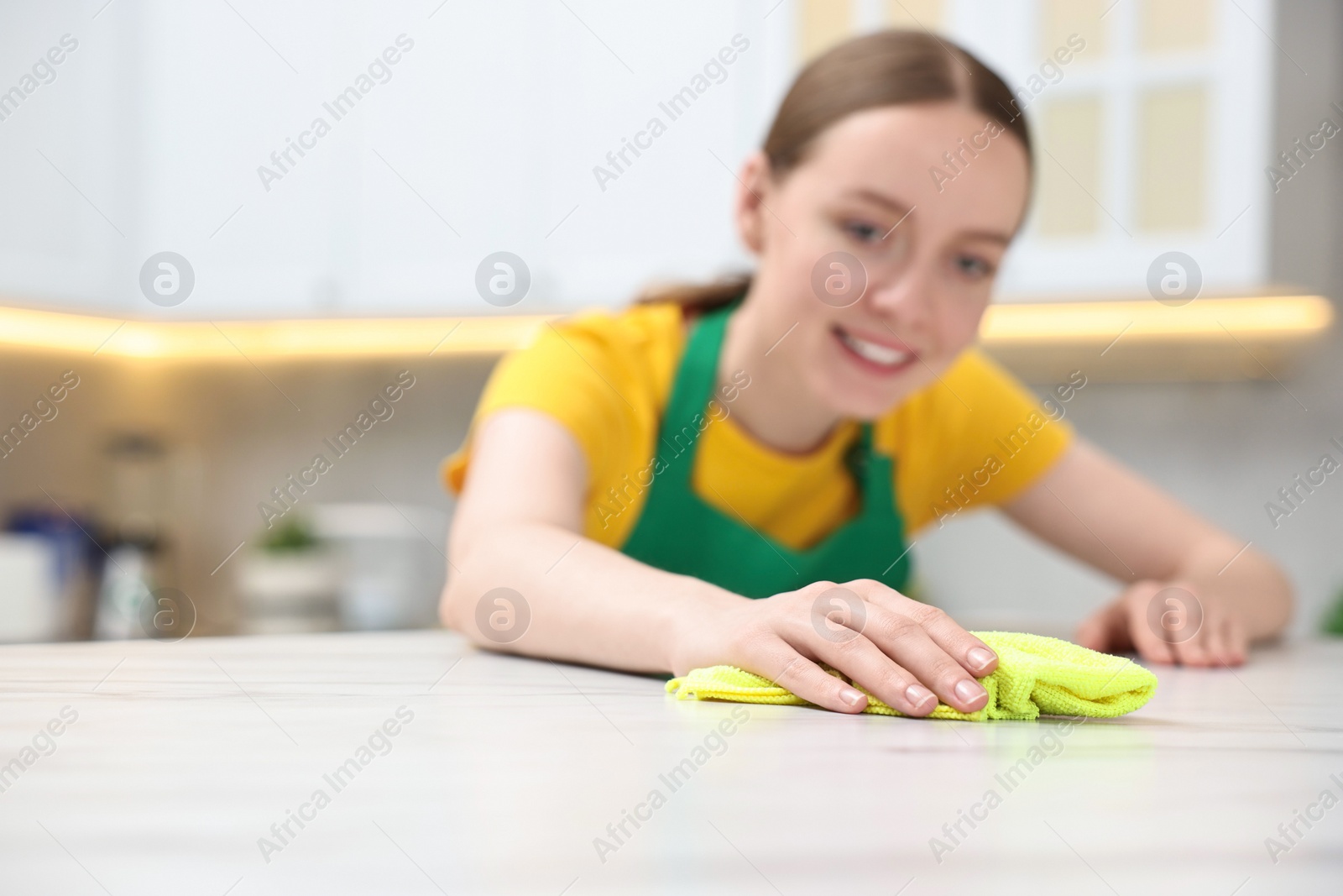Photo of Woman cleaning white marble table with rag in kitchen, selective focus. Space for text