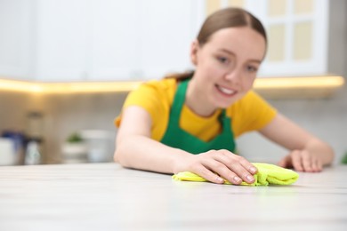 Woman cleaning white marble table with rag in kitchen, selective focus. Space for text