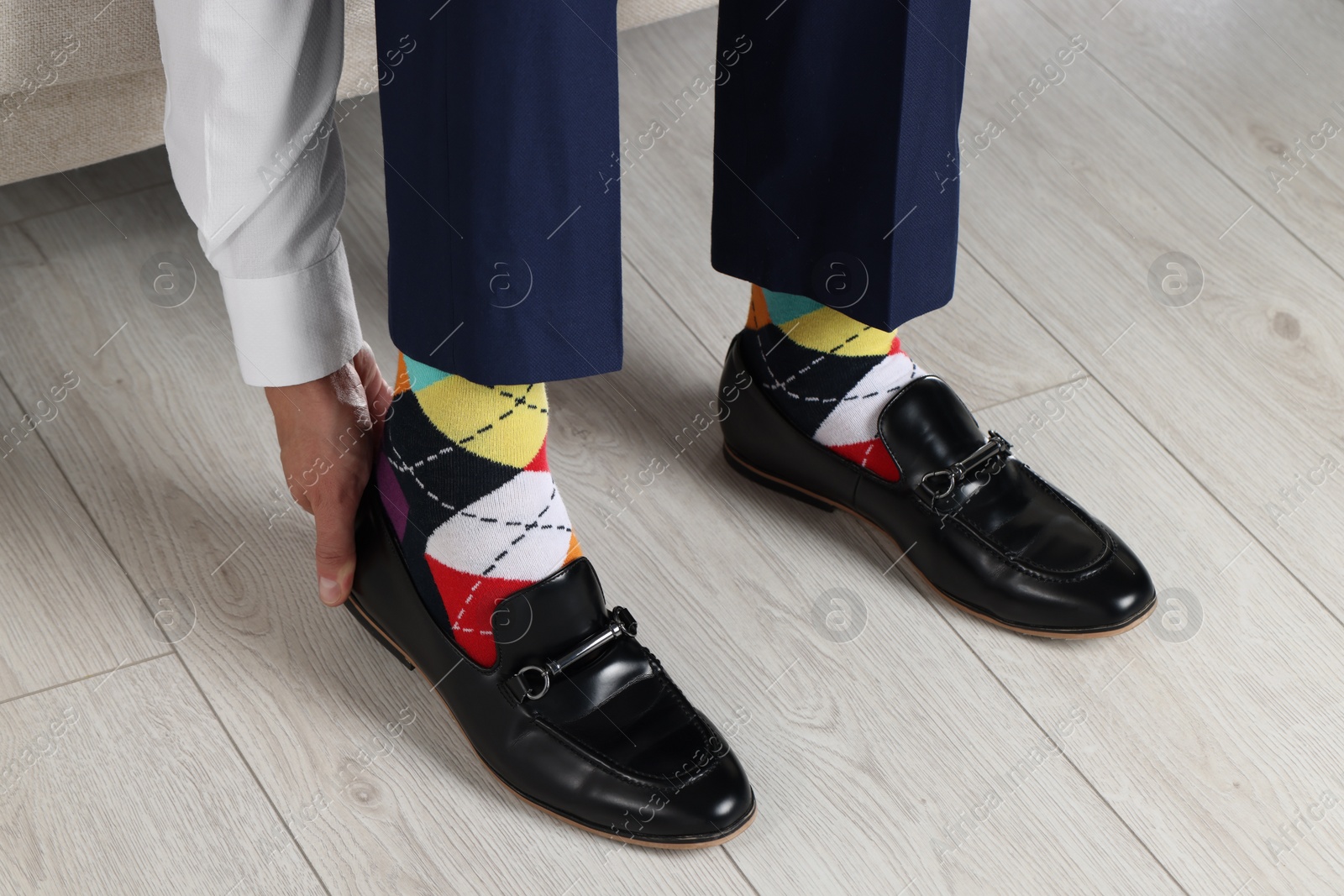 Photo of Man with colorful socks putting on stylish shoes indoors, closeup