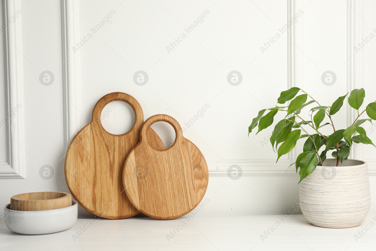 Photo of Wooden cutting boards, bowls and houseplant on white table