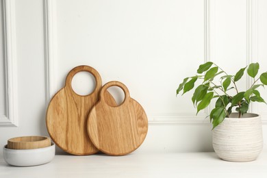 Photo of Wooden cutting boards, bowls and houseplant on white table