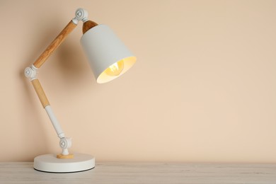 Photo of Stylish modern desk lamp on white wooden table near beige wall, space for text
