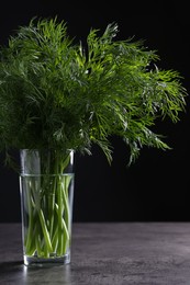 Photo of Fresh dill in glass on grey textured table against black background, closeup