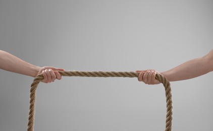 Photo of Dispute concept. Men pulling rope on light grey background, closeup