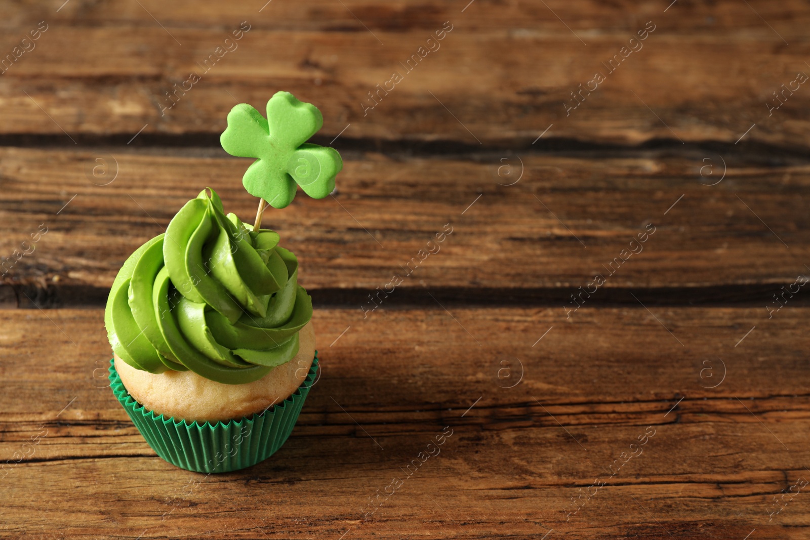 Photo of Delicious decorated cupcake on wooden table, space for text. St. Patrick's Day celebration