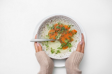 Photo of Woman with bowl of soup at white table, top view. Flu treatment