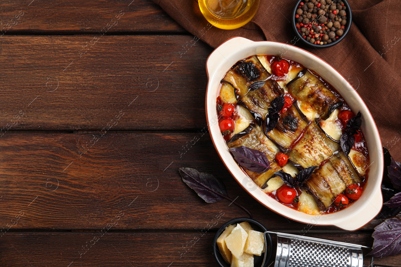 Photo of Tasty eggplant rolls with tomatoes and cheese in baking dish on wooden table, flat lay. Space for text