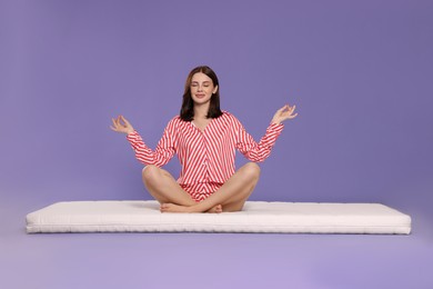 Photo of Young woman meditating on soft mattress against light purple background