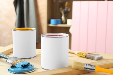 Cans of colorful paints and brushes on wooden table indoors