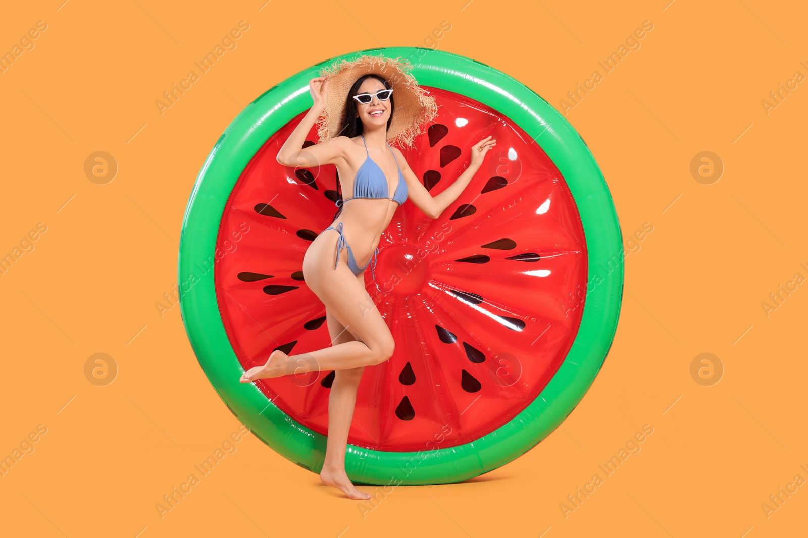 Photo of Happy young woman with beautiful suntan, hat, sunglasses and inflatable mattress against orange background