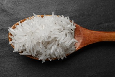 Photo of Raw basmati rice in wooden spoon on black background, top view