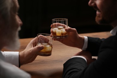 Men with glasses of whiskey talking at wooden table in bar
