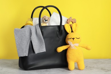 Photo of Mother's bag with baby's stuff on white marble table against yellow background