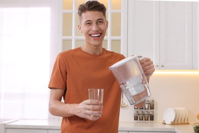 Happy man pouring water from filter jug into glass in kitchen