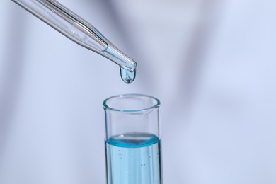 Dripping liquid from pipette into test tube on blurred background, closeup