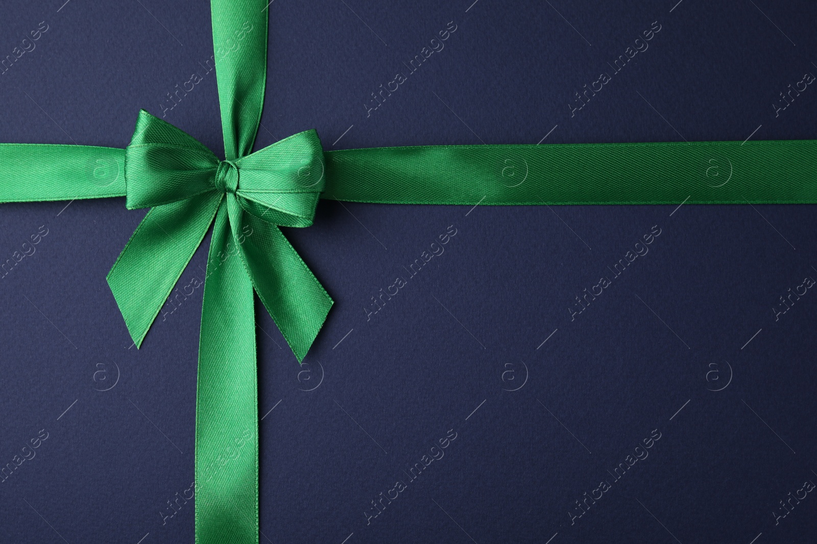 Photo of Green satin ribbon with bow on blue background, top view