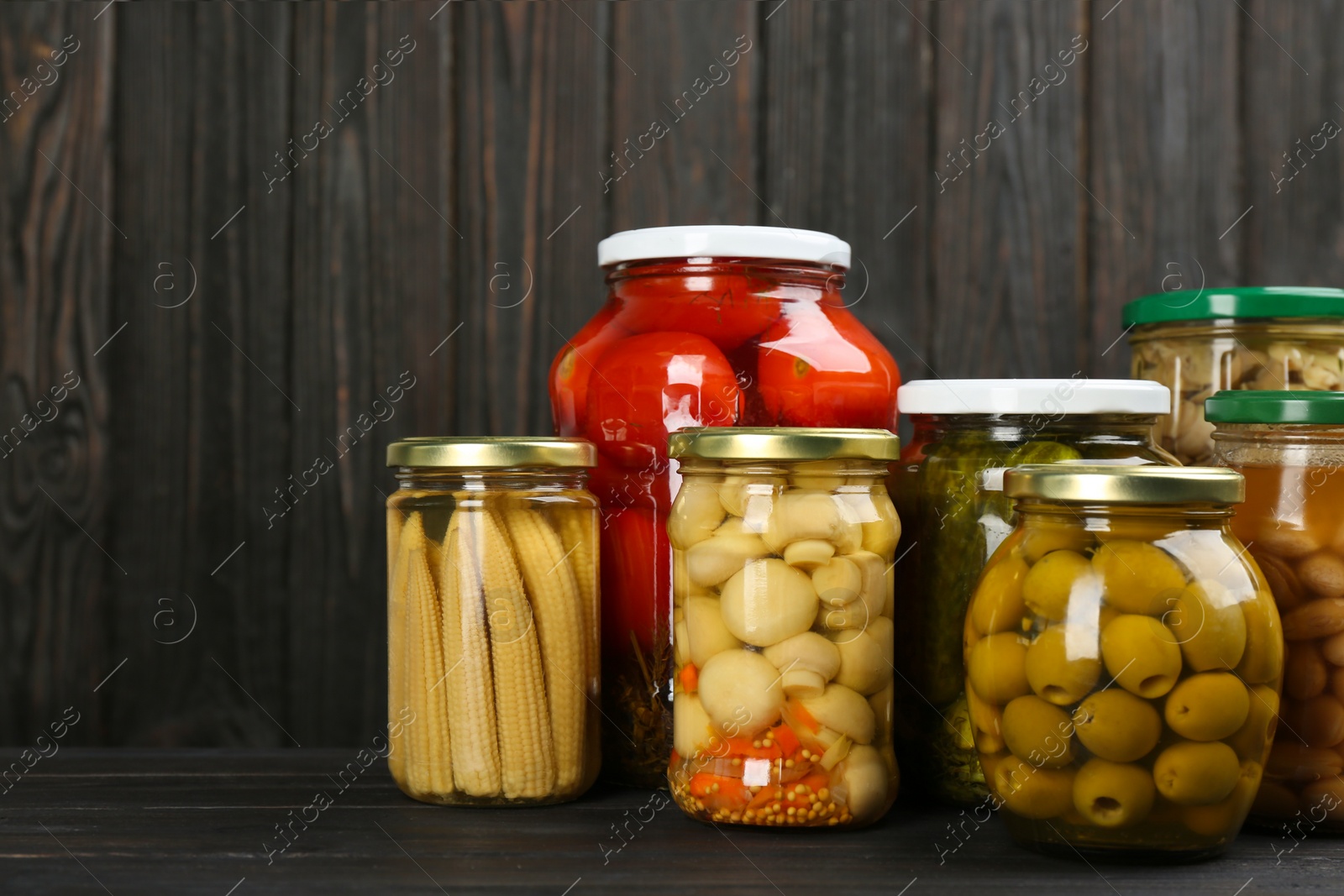 Photo of Glass jars with different pickled vegetables and mushrooms on wooden background