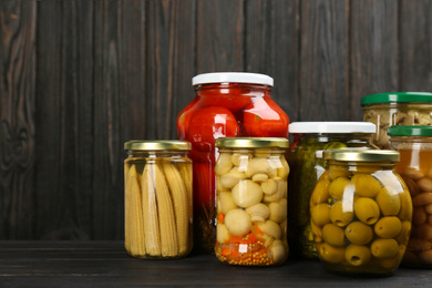 Photo of Glass jars with different pickled vegetables and mushrooms on wooden background