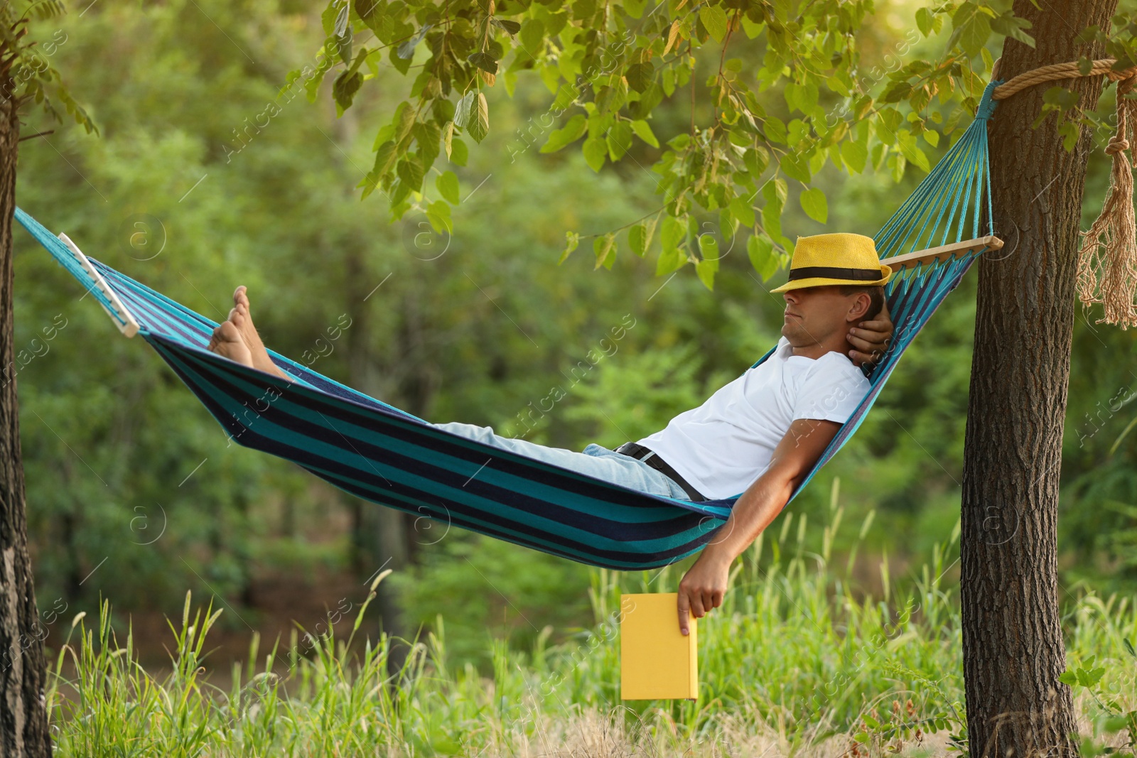 Photo of Man with book resting in comfortable hammock at green garden