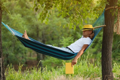 Man with book resting in comfortable hammock at green garden