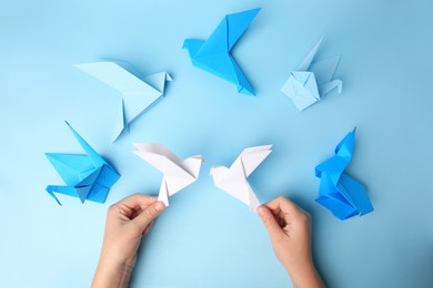 Origami art. Child holding paper birds on light blue background, closeup and top view