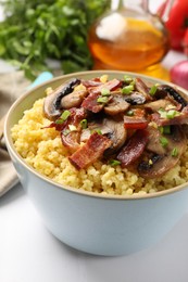 Photo of Tasty millet porridge with mushrooms, bacon and green onion in bowl on white table, closeup