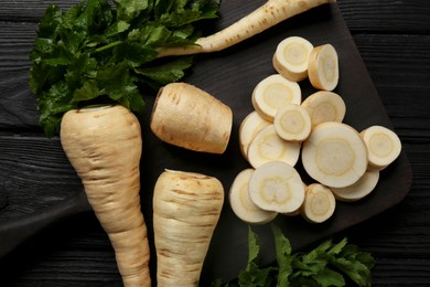 Whole and cut parsnips on black wooden table, flat lay