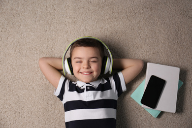 Photo of Cute little boy listening to audiobook on floor, top view