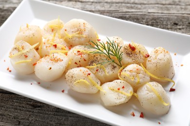 Photo of Raw scallops with spices, dill and lemon zest on wooden table, closeup
