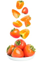 Image of Sweet ripe persimmons falling into bowl on white background