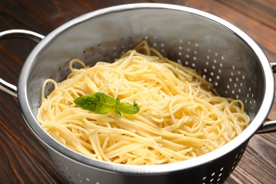 Cooked pasta in metal colander on wooden table, closeup